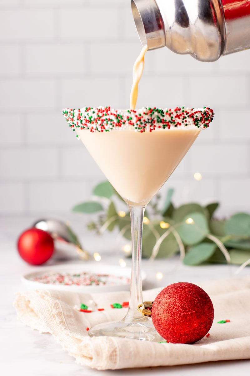Pouring a Christmas cocktail into a martini glass with sprinkles on the rim.