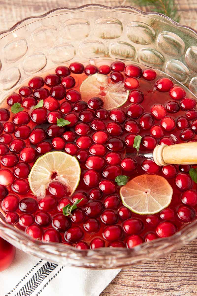 A punch bowl filled with Jingle Juice and fresh cranberries and lime slices floating on top.