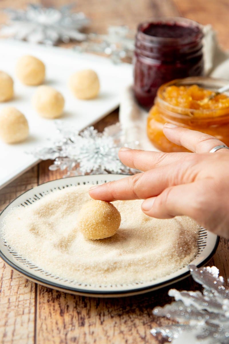 A hand rolling a ball of shortbread cookie dough in sugar for classic thumbprint cookies.