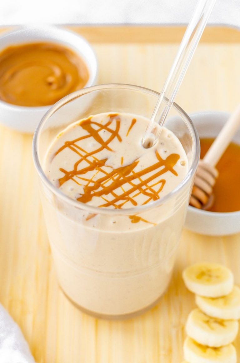 Close-up of finished smoothie with peanut butter drizzle and fresh ingredients around it.