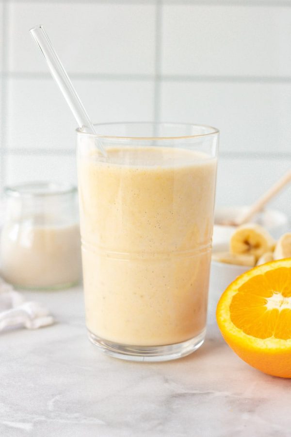 Close-up of orange smoothie in a glass with a glass straw.