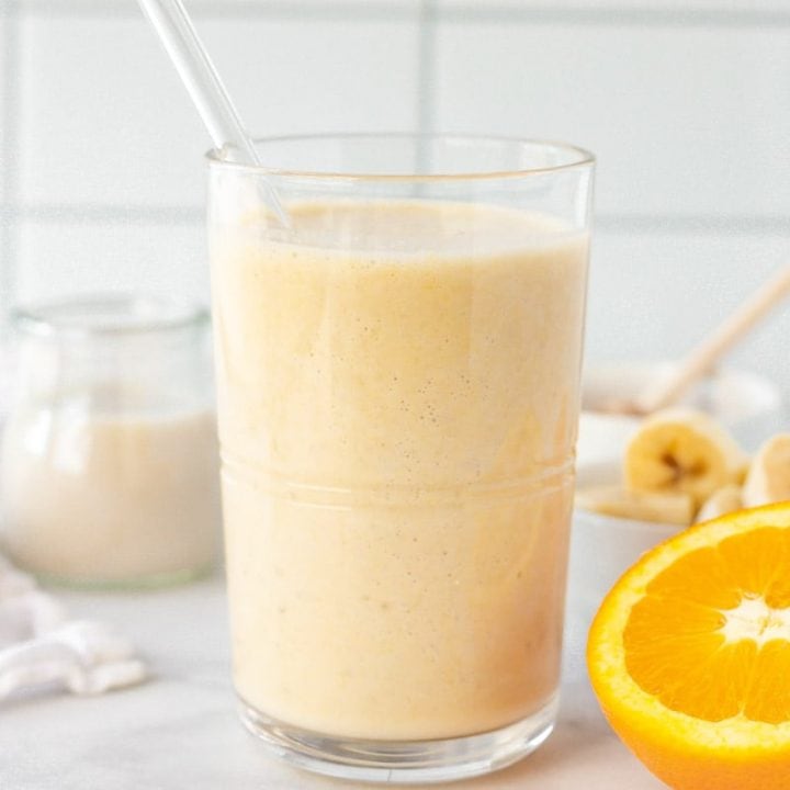 Close-up of orange smoothie in a glass with a glass straw.