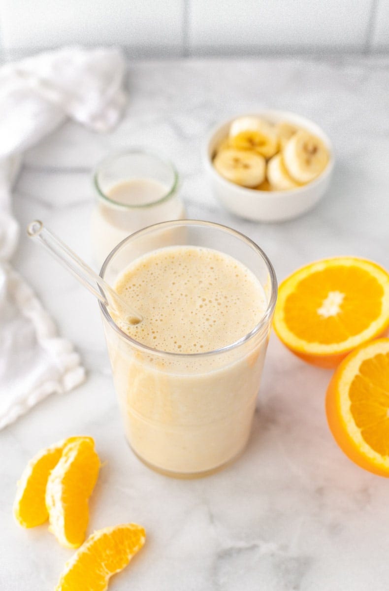 Blended smoothie served up in a glass with fresh fruit around it.