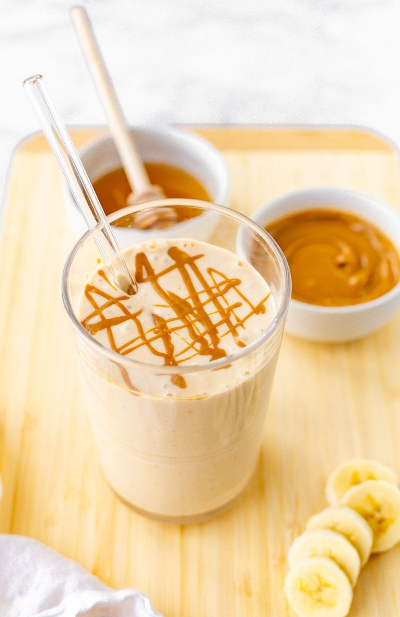 Peanut butter banana smoothie with a peanut butter drizzle on top and banana slices alongside.