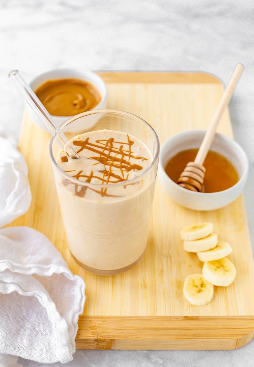 Overhead of smoothie on a cutting board with peanut butter, honey, and banana slices.