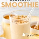 Close-up of smoothie with glass straw on cutting board with fresh ingredients. A text overlay reads, "Peanut Butter Banana Smoothie. Kid-Approved!"