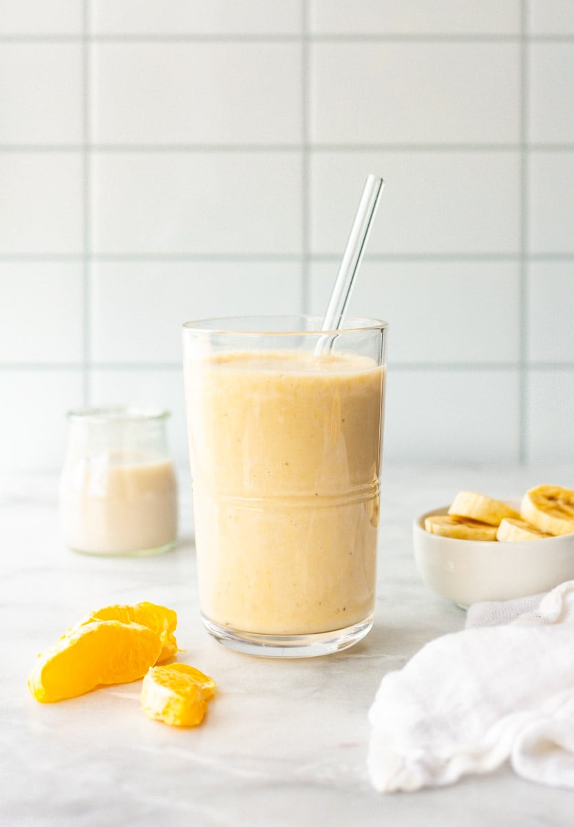 Orange smoothie in a glass with a glass straw.