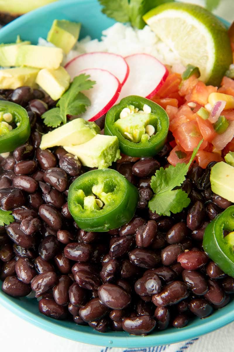 Close up of black beans in a bowl with fresh toppings such as radish slices, jalapeno slices, and avocado.