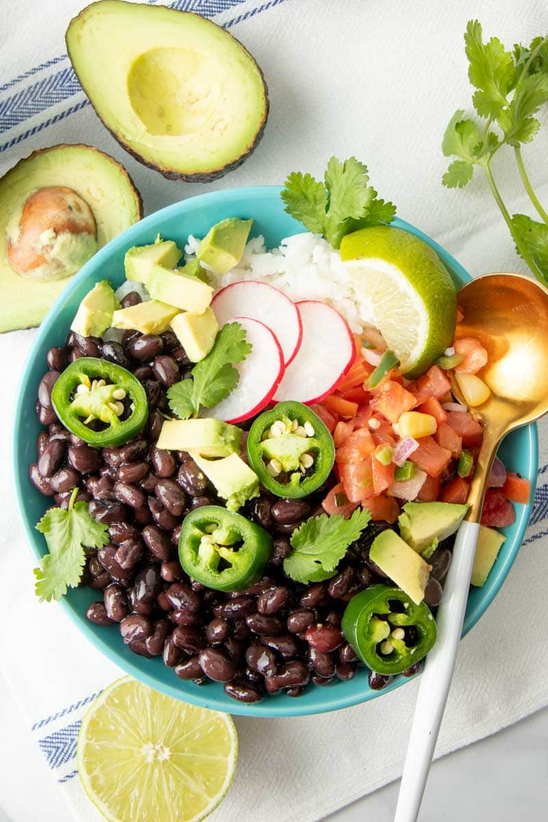 Overhead of a bowl of seasoned black beans topped with fresh salsa, jalapeno, cilantro, and avocado.