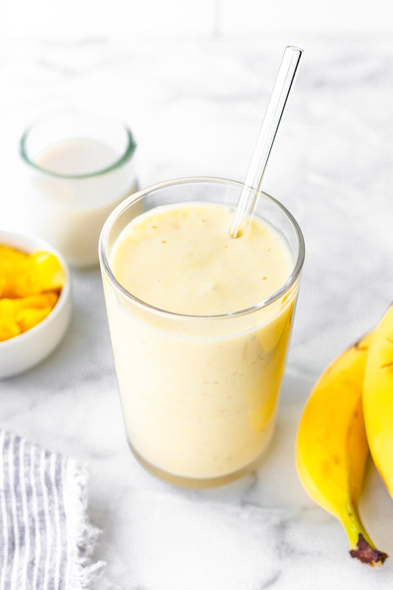 Finished smoothie in a glass with a glass straw and fresh fruit.