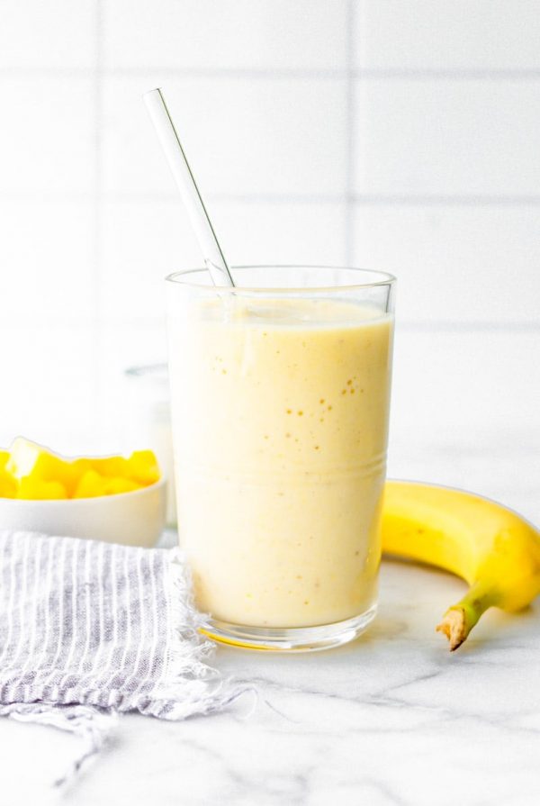 Coconut pineapple smoothie with a glass straw on a counter with fresh pineapple and banana.