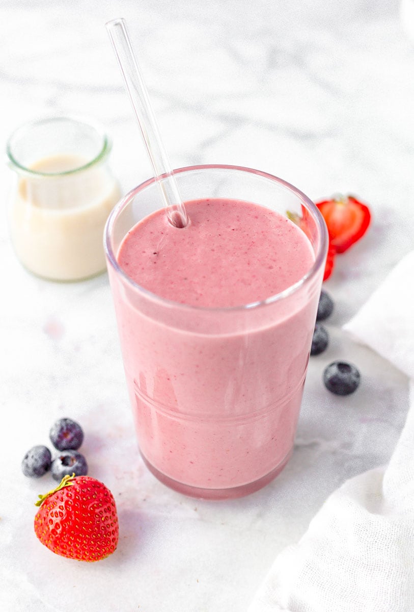 Berry smoothie in a glass with glass straw and fresh berries.