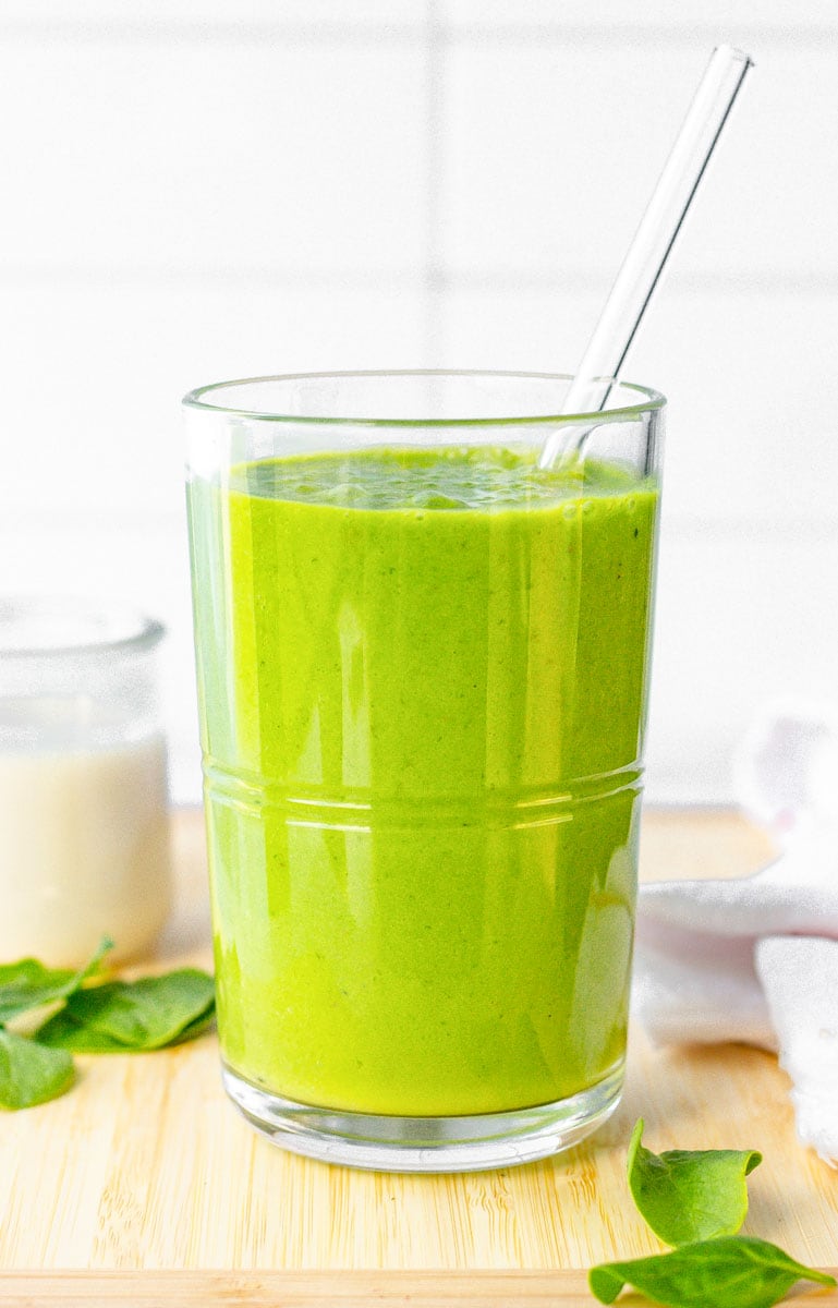 Green smoothie close up on a cutting board with a glass straw in it.