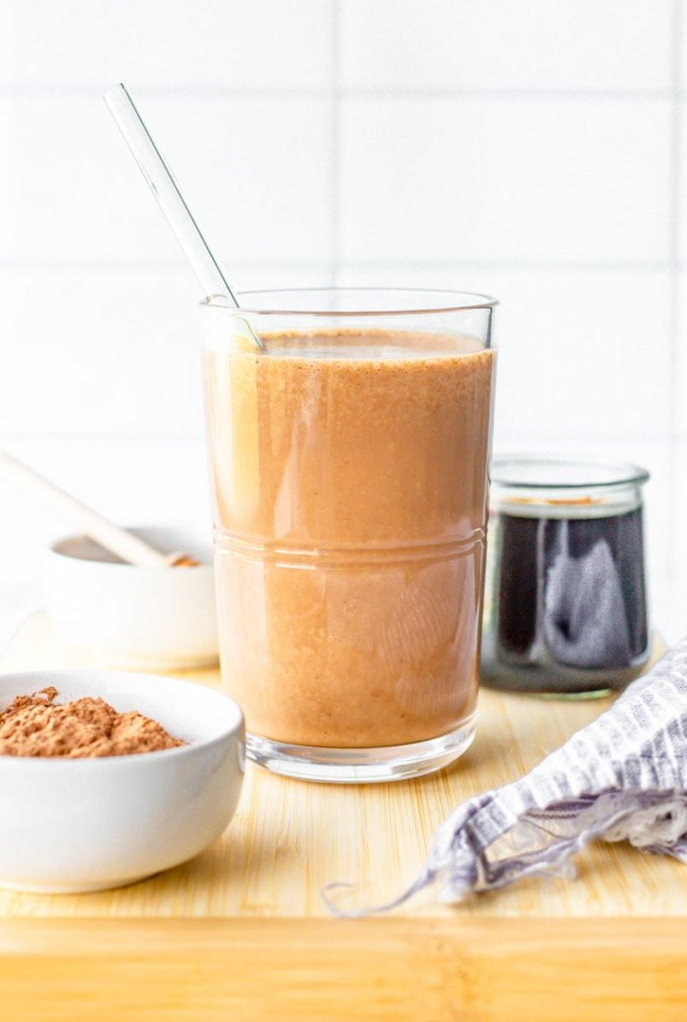 Chocolate coffee smoothie with glass straw on cutting board with ingredients.