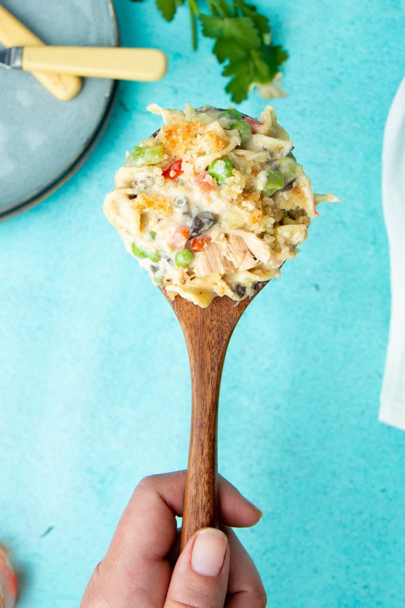 Hand holding up a wooden spoon with a scoop of tuna casserole on it.