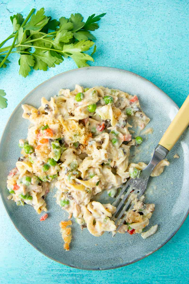 Overhead of tuna noodle casserole on a plate with a fork and fresh parsley.