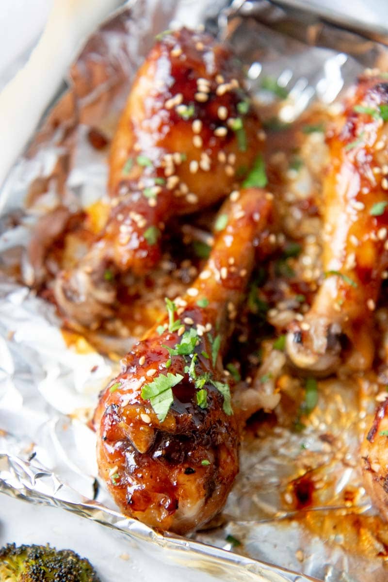 Close-up of a sticky chicken drumstick garnished with chopped fresh cilantro on a foil lined sheet pan.