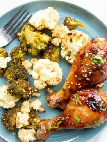 A blue dinner plate filled with two baked drumsticks and roasted broccoli and cauliflower.
