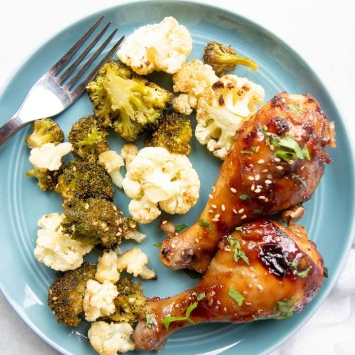 A blue dinner plate filled with two baked drumsticks and roasted broccoli and cauliflower.