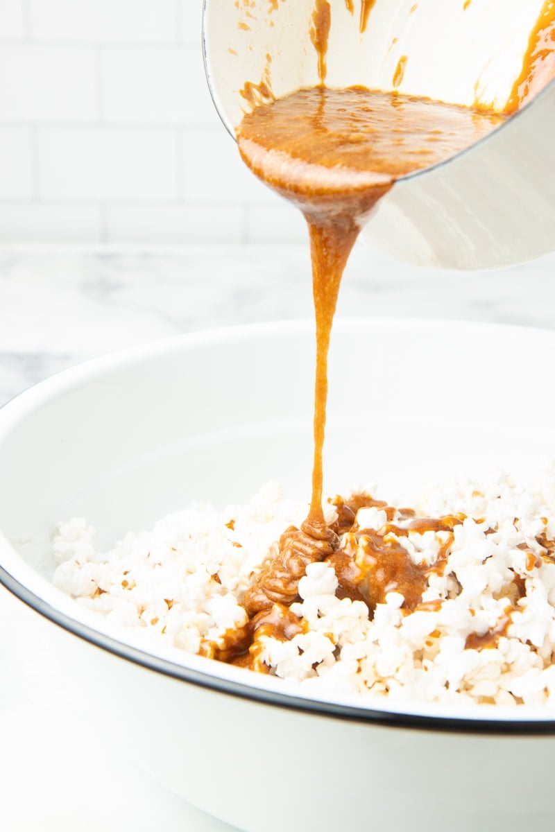 Pouring hot caramel topping into a big bowl of fresh popped popcorn.