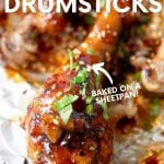 Close-up of a sticky chicken drumstick garnished with chopped fresh cilantro on a foil lined sheet pan. A text overlay reads, "Sticky Chicken Drumsticks. Baked on a Sheetpan!"