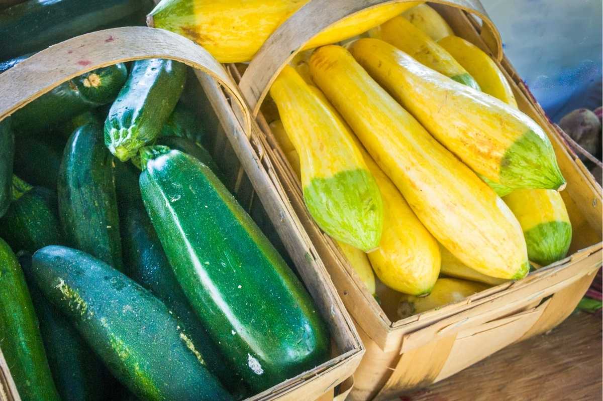 Two wooden baskets with handles filled with yellow summer squash on the right and green zucchini on the left.