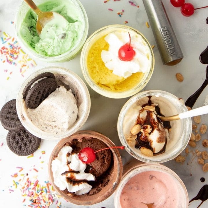Overhead shot of various flavors of mason jar ice cream, with various toppings around the jars. Flavors include strawberry, peanut butter, cookies n cream, lemon, chocolate, and mint chocolate chip.