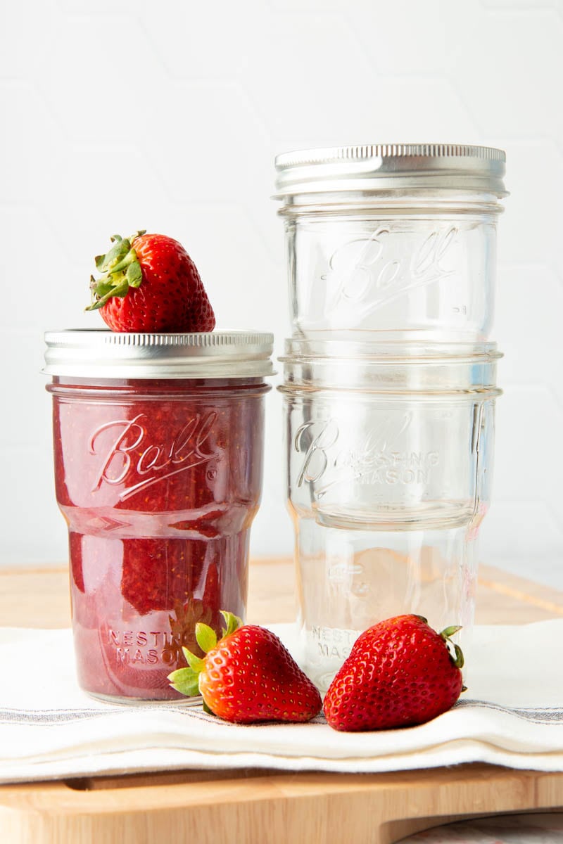 Strawberry jam in a glass jar sits next to two nested glass jars