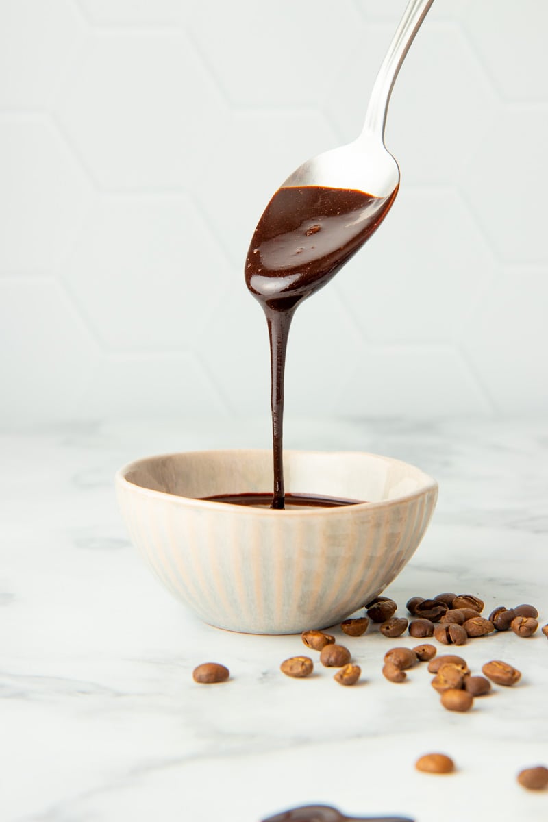 A spoon drizzles diy mocha syrup back into a small bowl of the homemade syrup.
