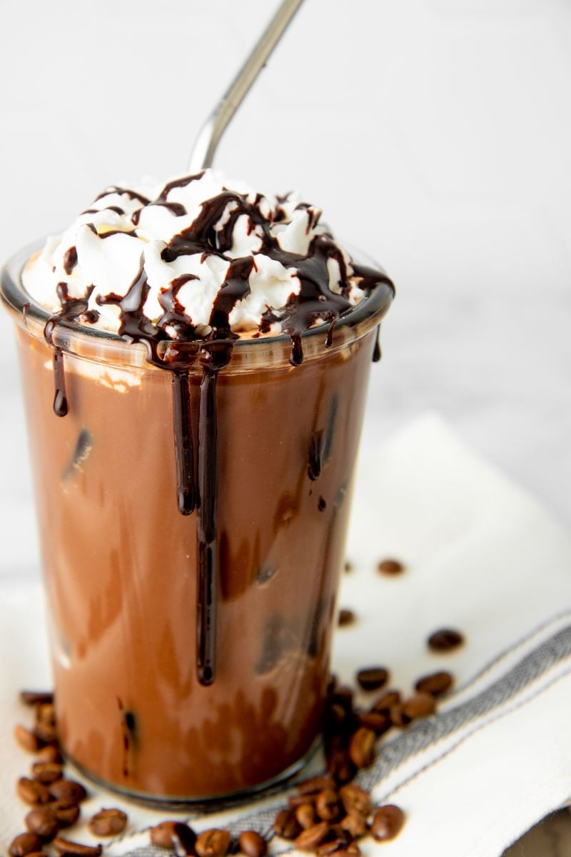Close-up of homemade iced mocha in a glass with ice garnished with whipped cream and a mocha syrup drizzle.