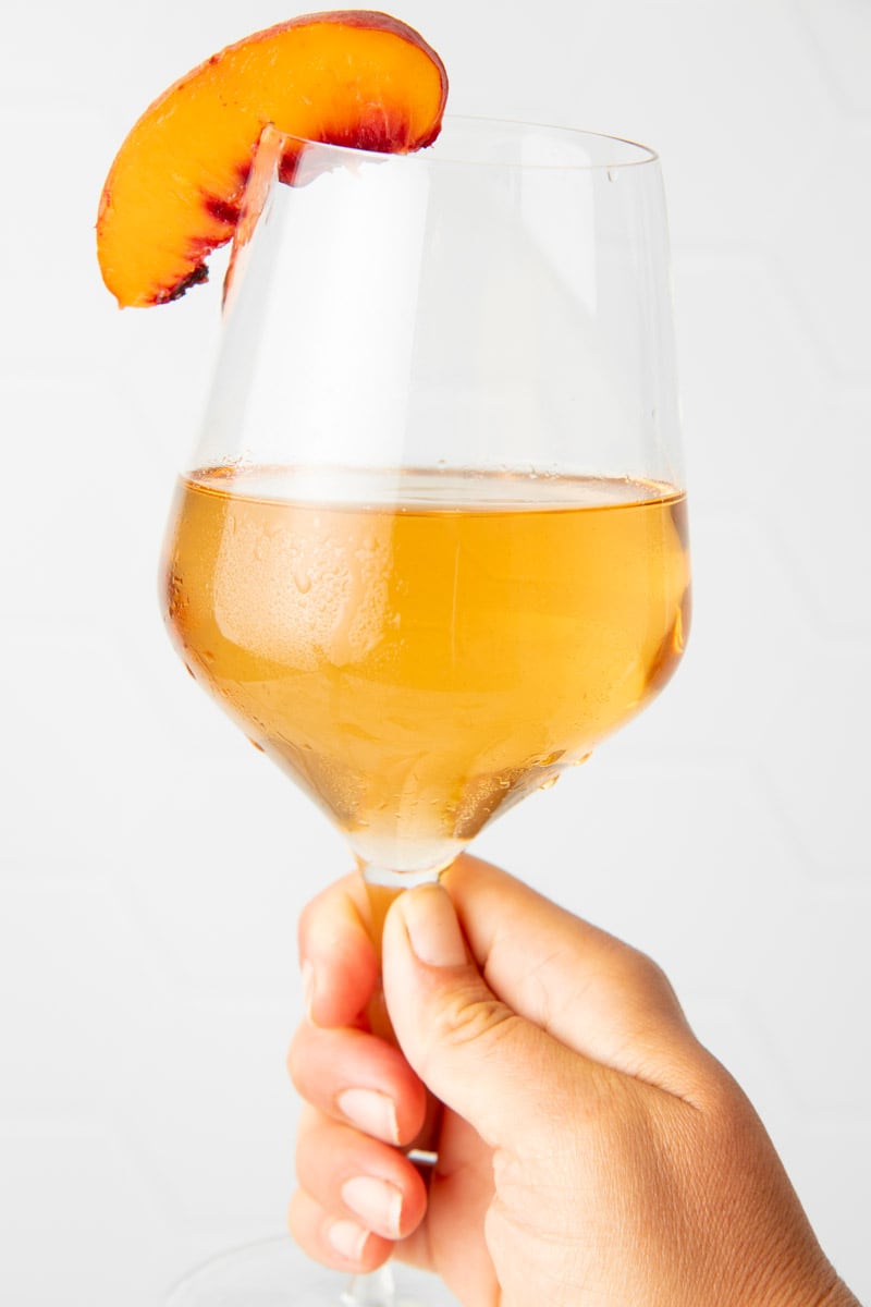 A hand holds up a chilled glass of homemade peach wine.