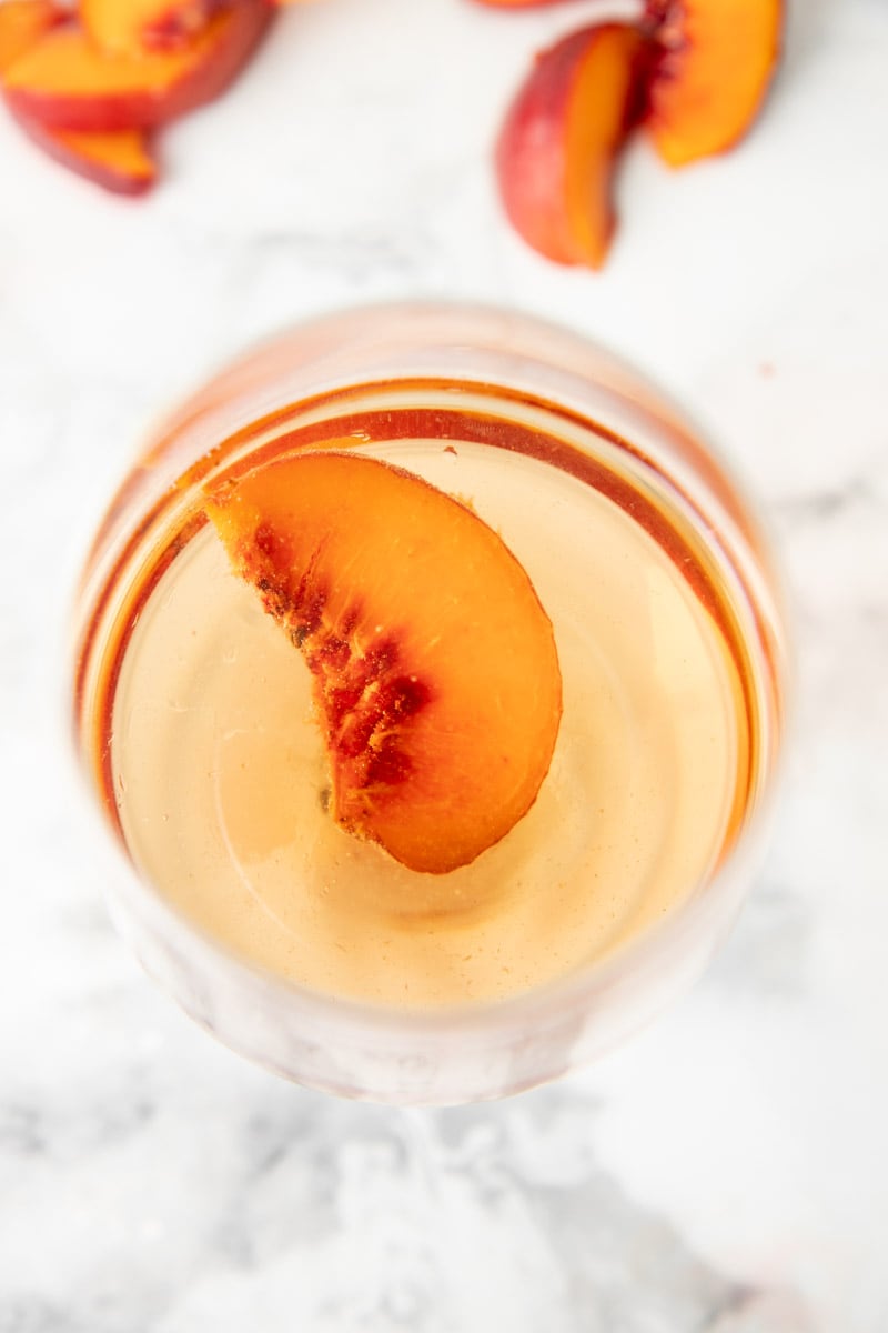 Overhead of clear peach wine in a glass with a fresh peach slice.