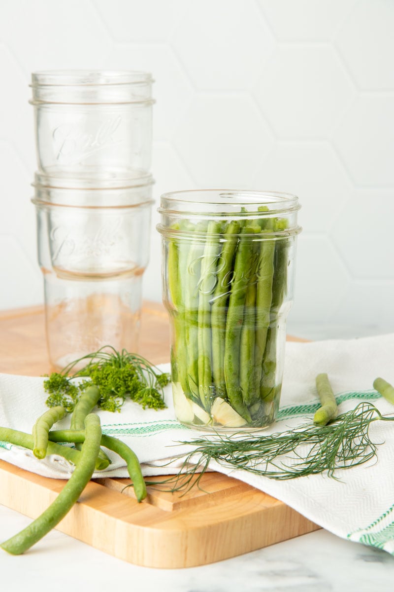 Green beans are packed into a glass jar. Two empty glass jars are nested behind the full jar.