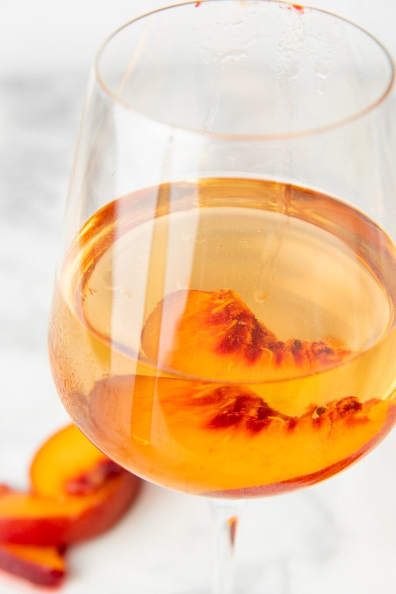 Close up of a glass of peach wine with a fresh peach slice in the glass.