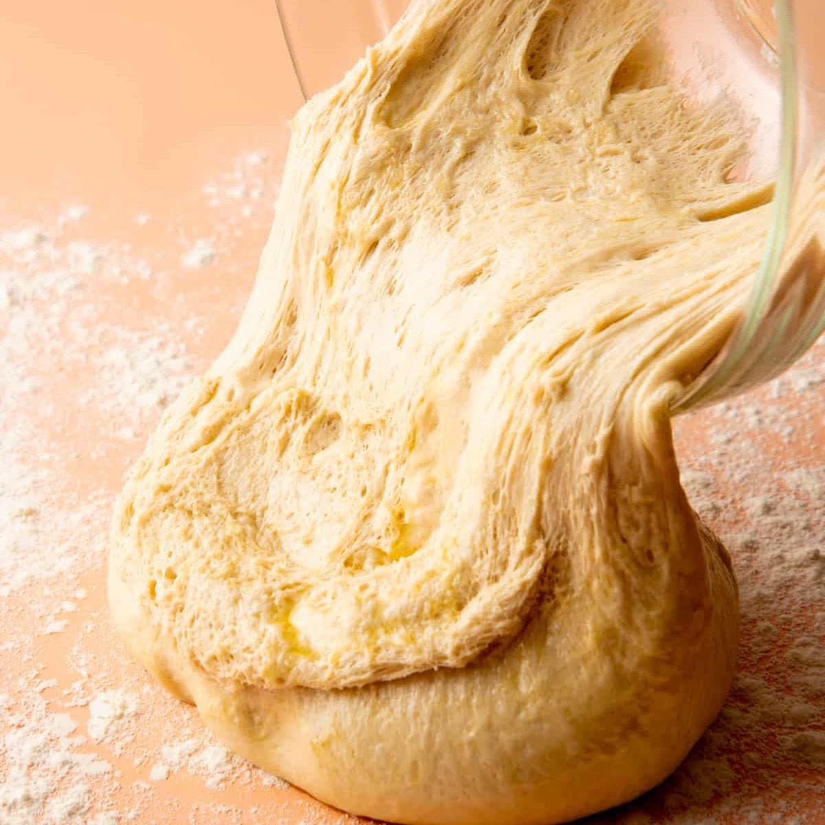 Risen sandwich bread dough being turned out onto a floured surface.