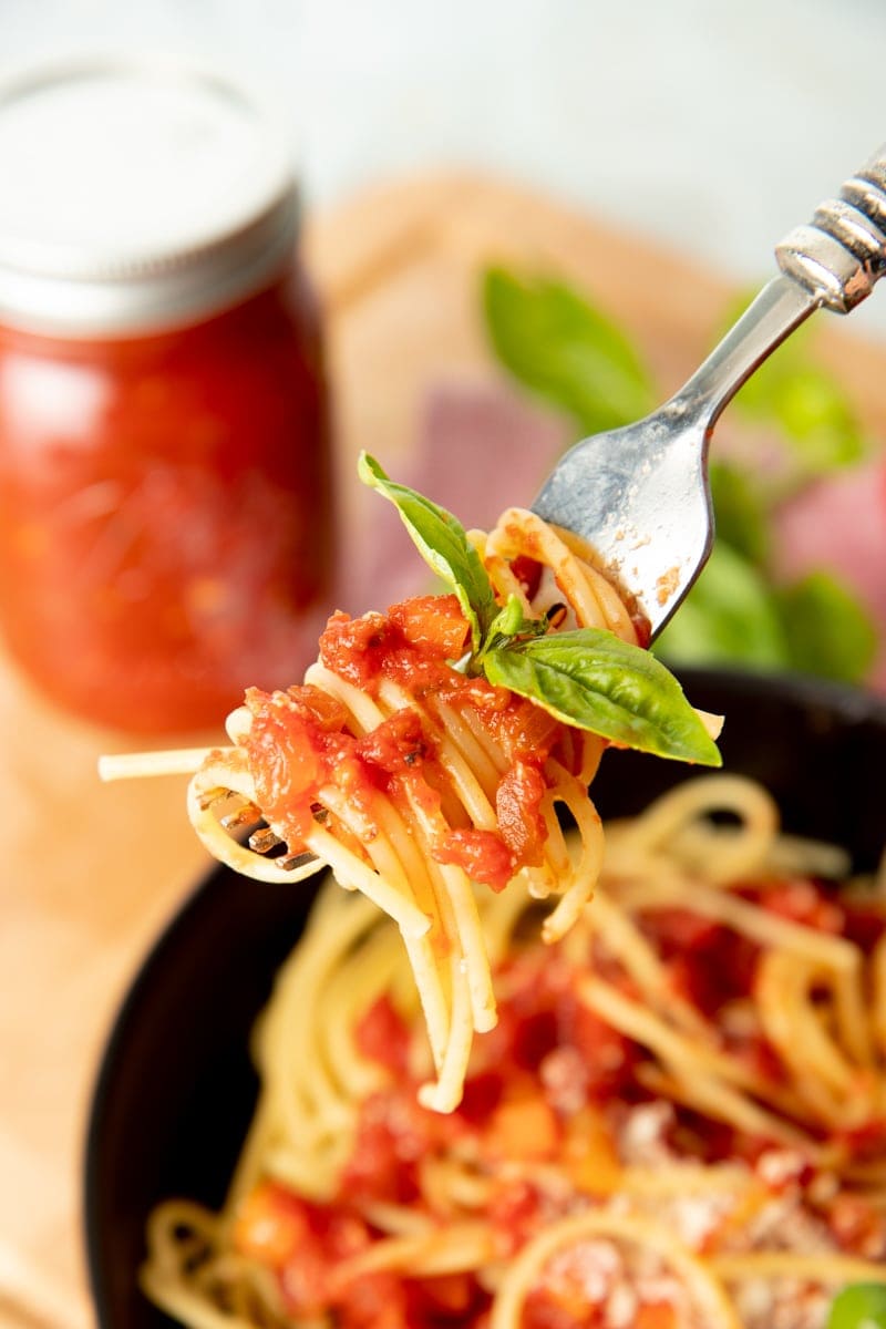 A fork holds a bite of spaghetti with sauce and fresh basil
