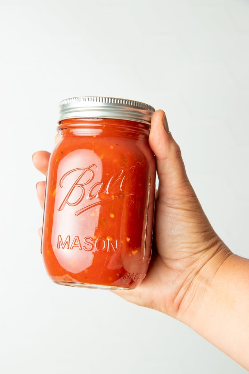 A hand holds out a jar of homemade spaghetti sauce