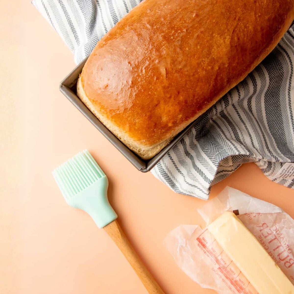 A loaf of fresh baked sandwich bread with a pastry brush and stick of butter
