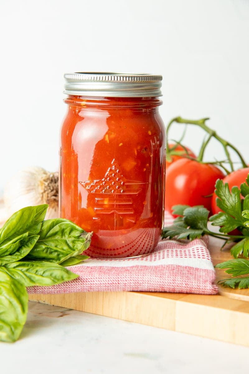 A full glass jar of spaghetti sauce sits on a dish towel on a cutting board.