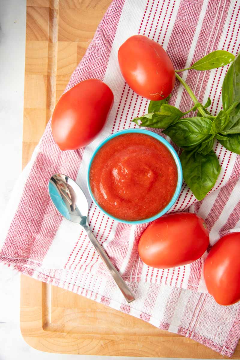 Overhead of a small bowl of tomato puree surrounded by fresh roma tomatoes and basil.