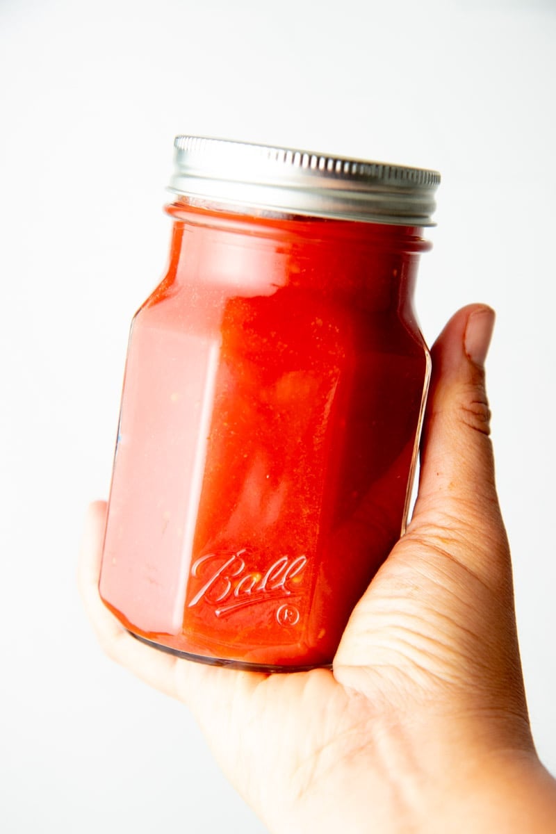 A hand holds a Ball jar of canned tomato sauce.