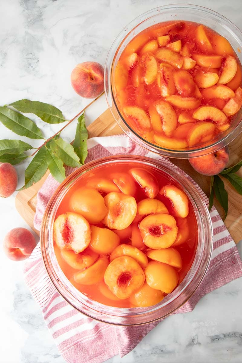 Overhead of two bowls filled with cut halves and cut slices in juice or syrup.