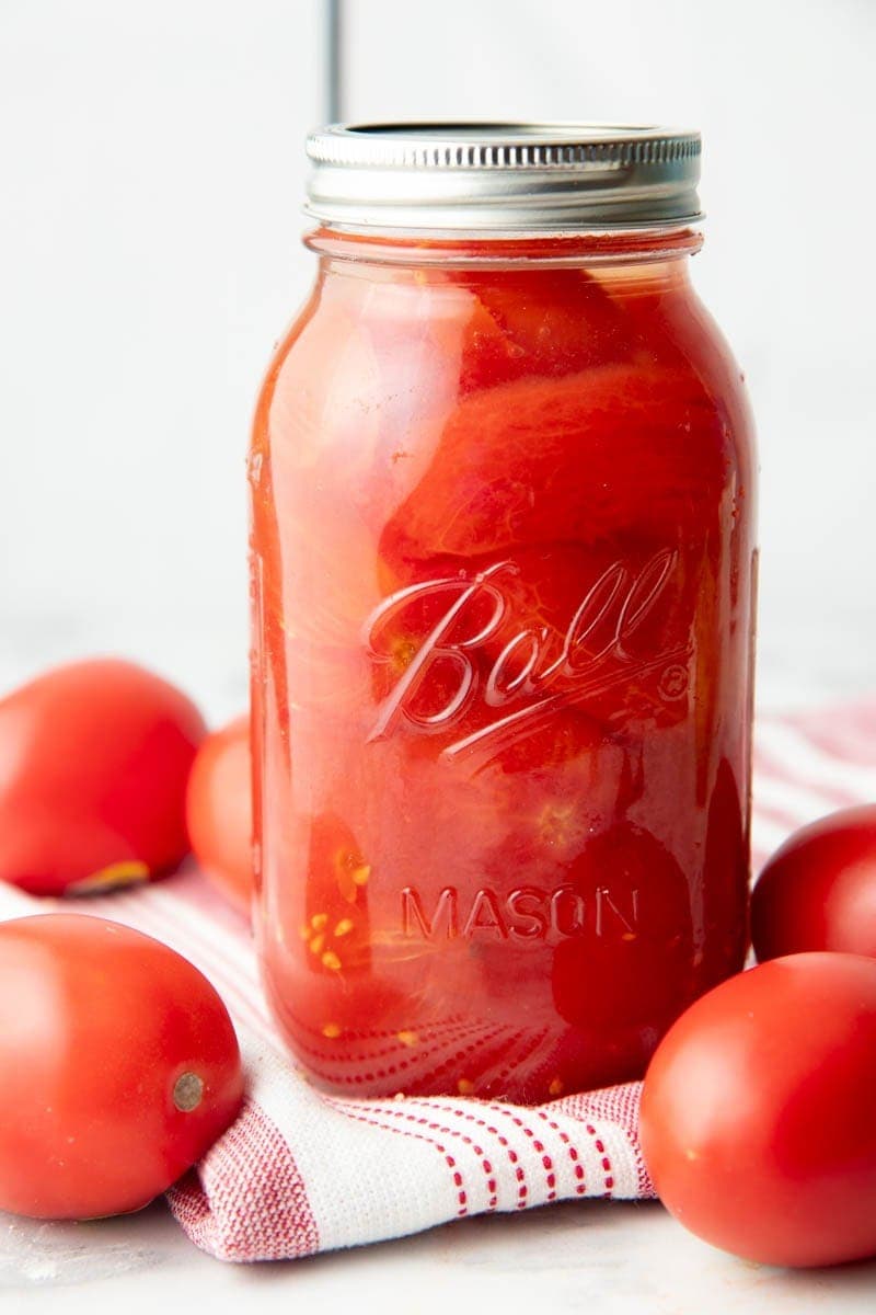 Close-up of a finished jar on a kitchen linen with fresh tomatoes around.