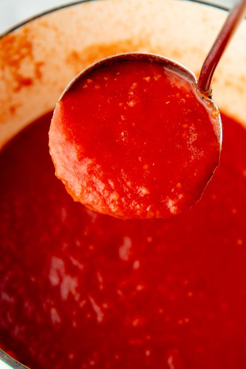 Close-up of a ladle full of tomato sauce above the pot of sauce.