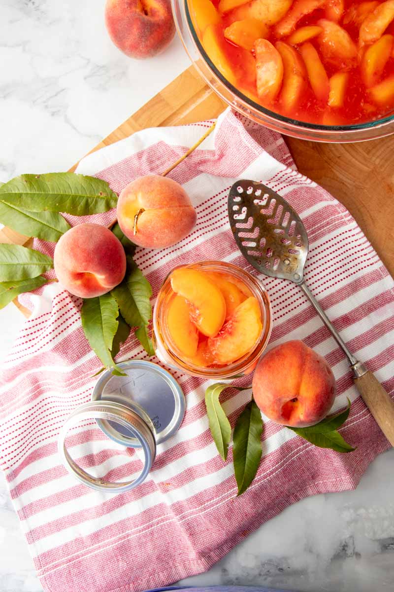 A filled half-pint jar sits beside a bowl of peach slices on a cutting board.