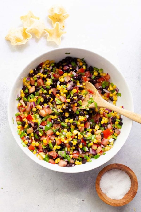 Overhead of a white serving bowl with black bean and corn salsa and a wooden spoon in it.