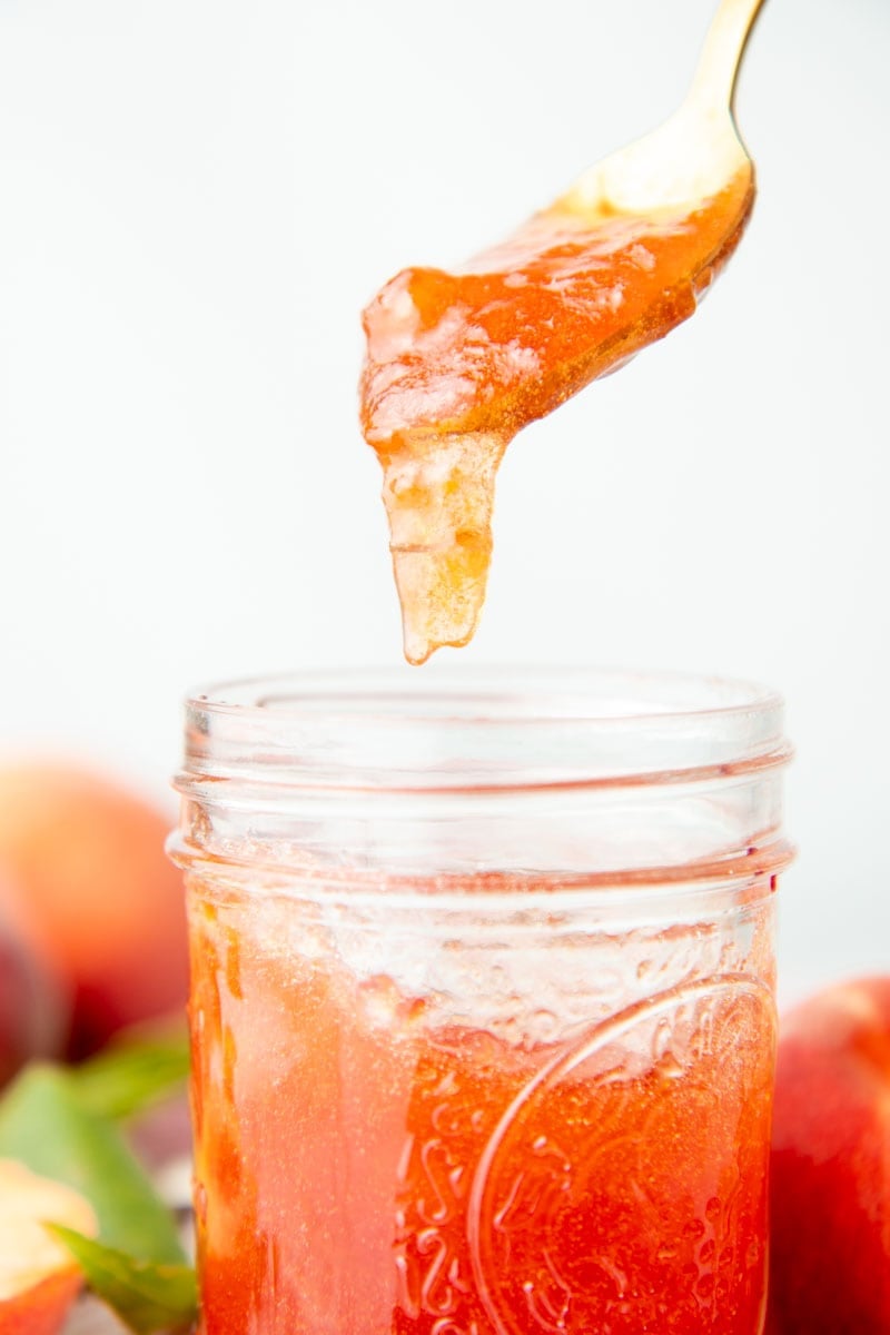 Jam drips off a spoon, back into its jar