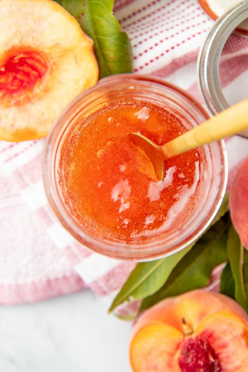 A spoon rests in a jar of rosy-orange jam