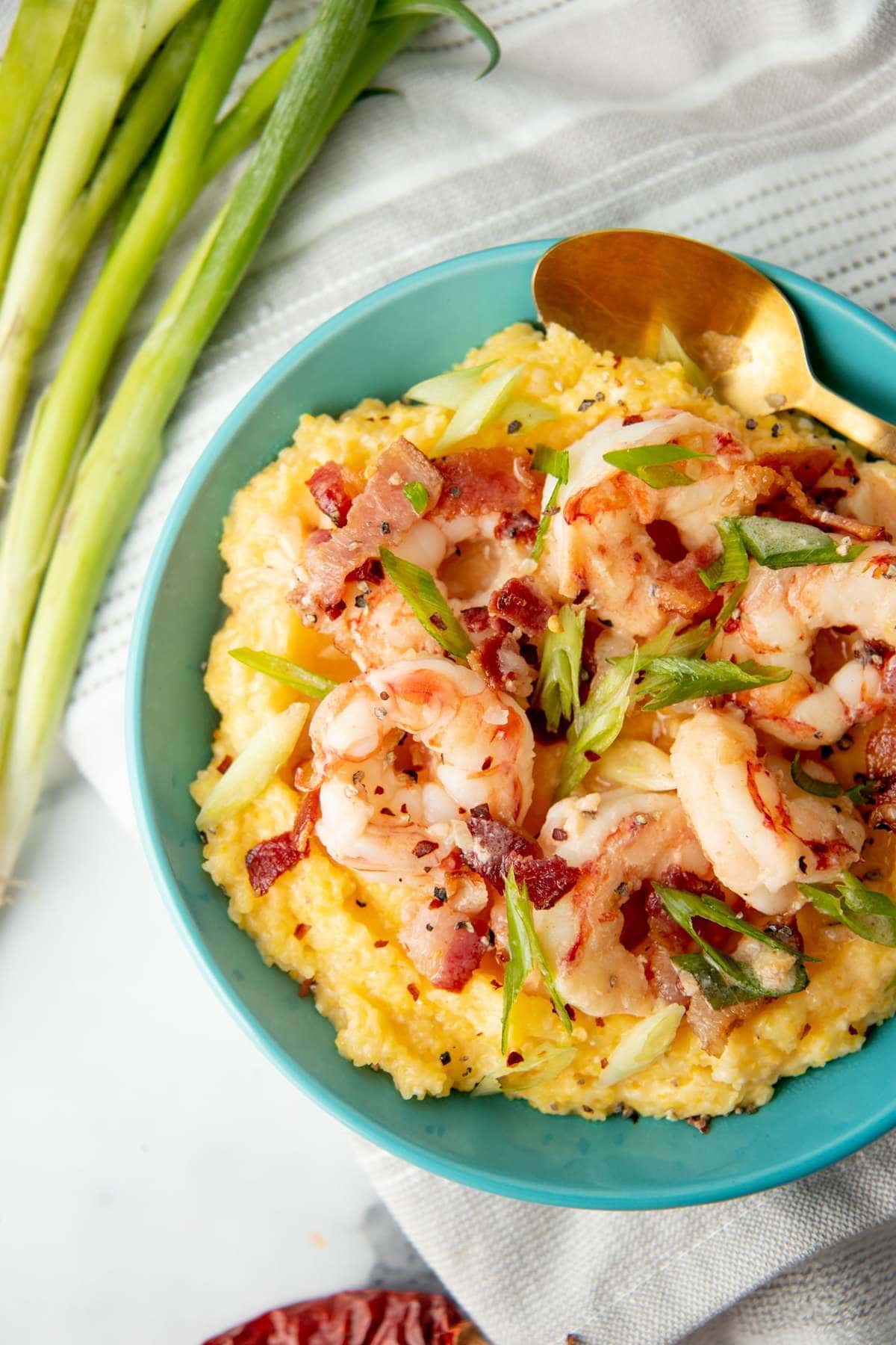 Shrimp and grits for one in a teal bowl with a gold spoon.