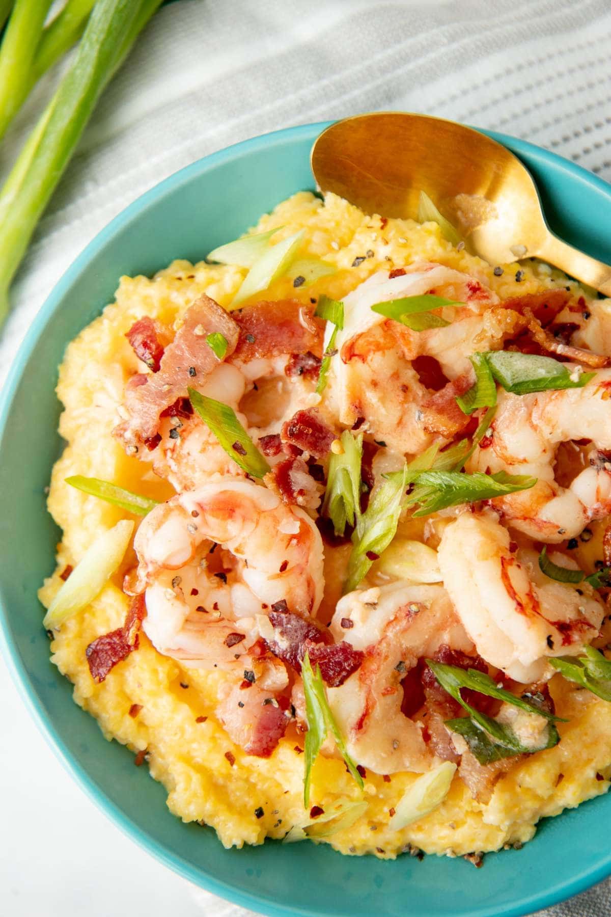 Close view of a bowl of shrimp and grits garnished with crumbled bacon and sliced green onion.